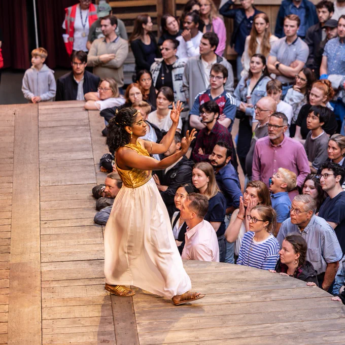 Nadia Nadarajah as Cleopatra in Antony & Cleopatra (2024). 

An actor wearing a gold dress on stage at the Globe Theatre, performing in front of an attentive audience.