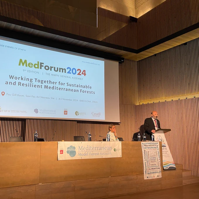 Man speaking at a podium. Med Forum 2024 projected in background.