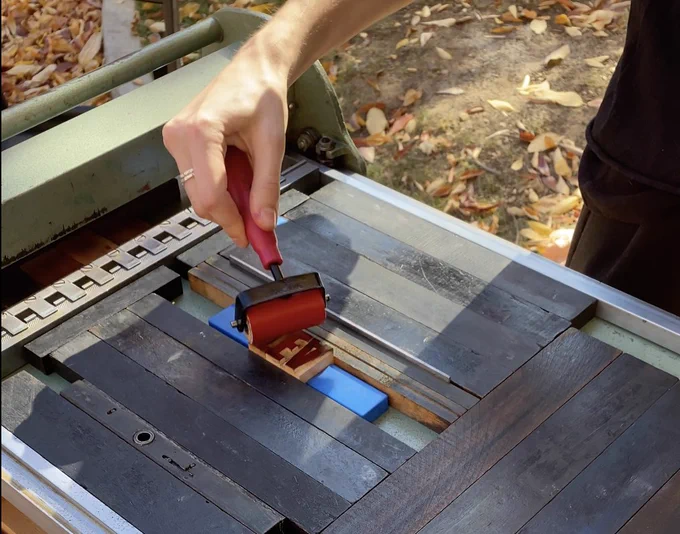 Person adding red ink to letterpress type on a metal letterpress.