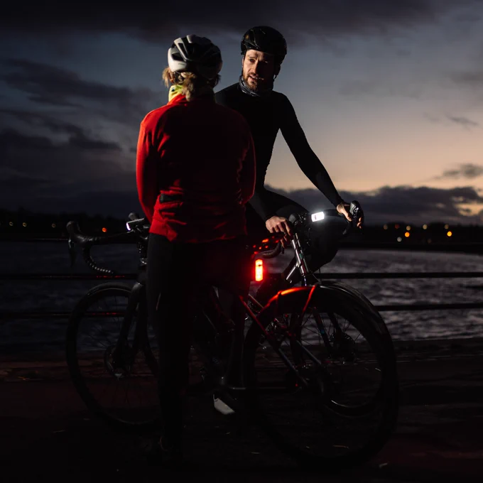 Two cyclists having a conversation on a dark evening, with SeeSense lights ensuring they are visible