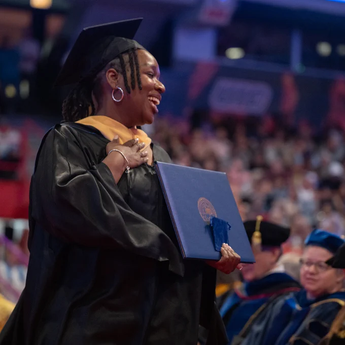 A graduate smiles while holding a diploma