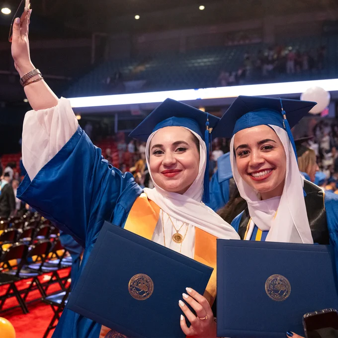 Two graduates hold diplomas