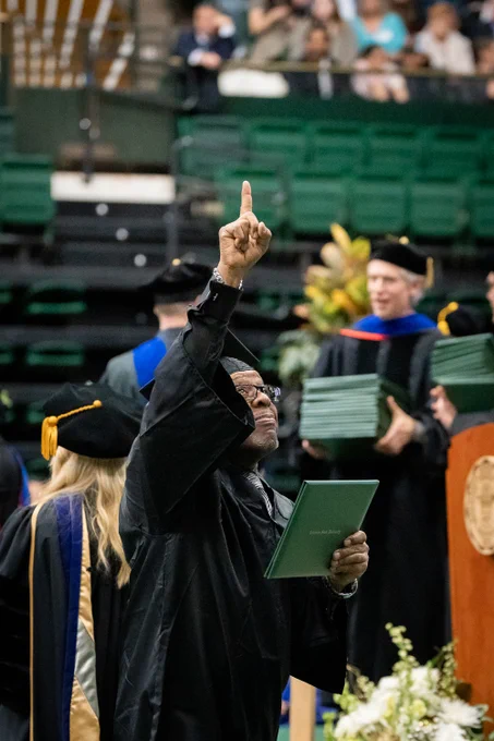 A graduate pointing their finger in the air and holding their diploma during graduation in Moby Arena.