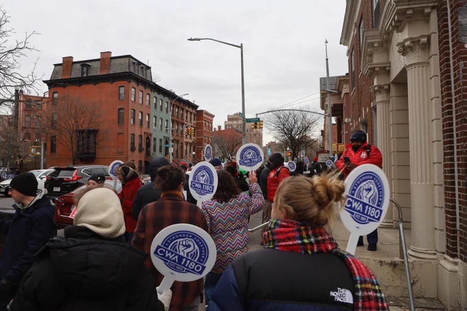 Picture of rally- people walking holding signs.