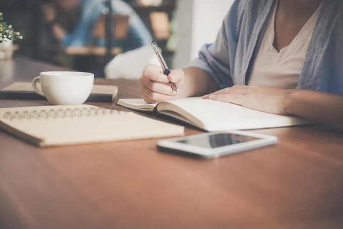 Person sitting at a table writing with pen and paper