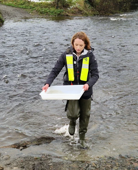 Farming for Water's Mairead Shore collecting water samples from a river, wearing a safety life jacket and waders.