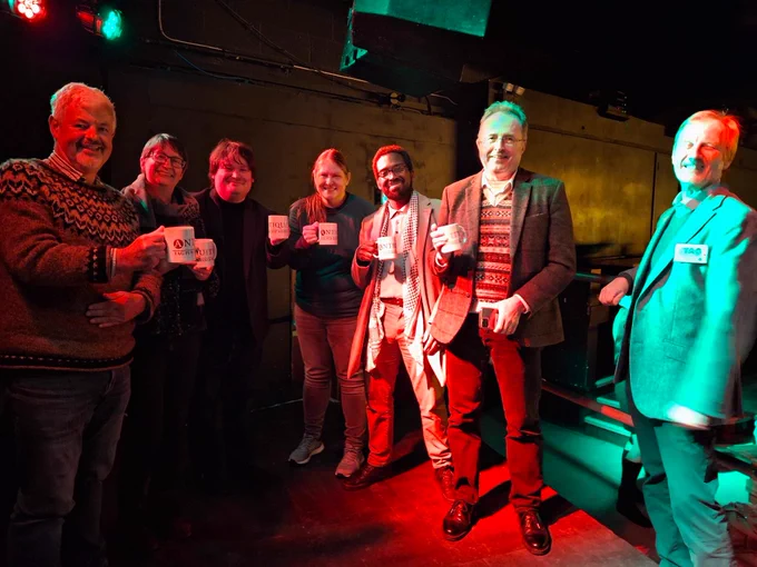 A team of six people smiling and holding Antiquity mugs. Incoming Antiquity editor Prof. Robin Skeates stands next to them smiling