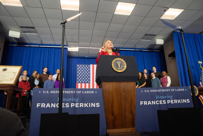AFL-CIO President Liz Shuler speaking at a podium at the Frances Perkins homestead national monument dedication ceremony at the Department of Labor headquarters in a Washington, DC