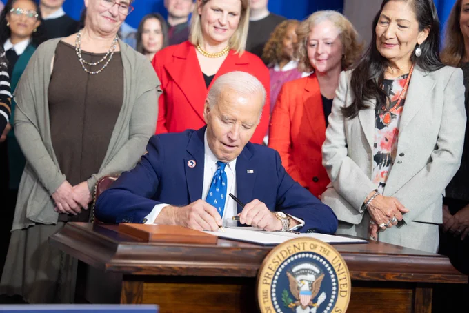 President Joe Biden at a desk signing the Frances Perkins homestead national monument dedication ceremony.