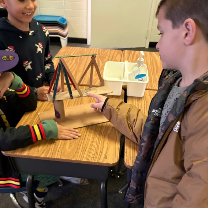 Students building a bridge out of cardboard, paper towel tube and popsicle sticks