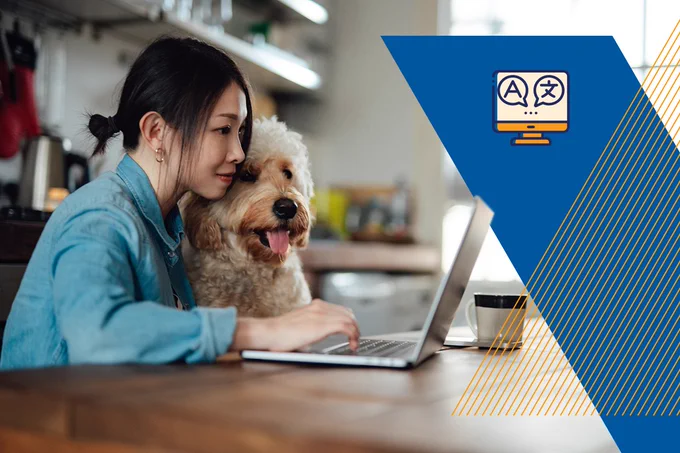 Image Description: A woman sitting with her dog in her lap at a kitchen table and looking at her computer.
