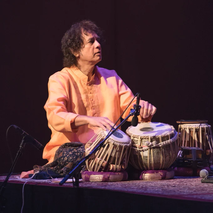 Zakir Hussain plays a tablā onstage in the MIM Music Theater.