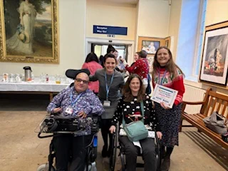 A picture of four colleagues celebrating their award certificate in a reception hall. They are smiling and wearing festive jumpers.