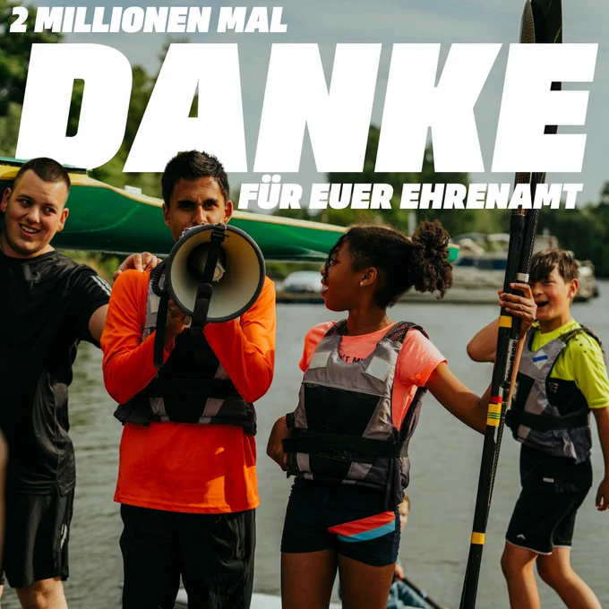 Das Bild zeigt eine Gruppe von Menschen, die sich auf einer Bootsanlegestelle versammelt haben. Eine Person hält ein Megafon in der Hand und spricht in dieses hinein, während die anderen Gruppenmitglieder aufmerksam zuhören. Das Bild hat eine Überschrift, die "2 Millionen Mal Danke für Euer Ehrenamt" lautet.
