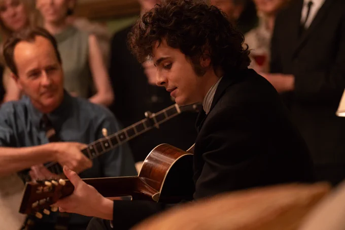 Timothée Chalamet as Bob Dylan in A Complete Unknown, playing a guitar whilst people watch rapturously. 