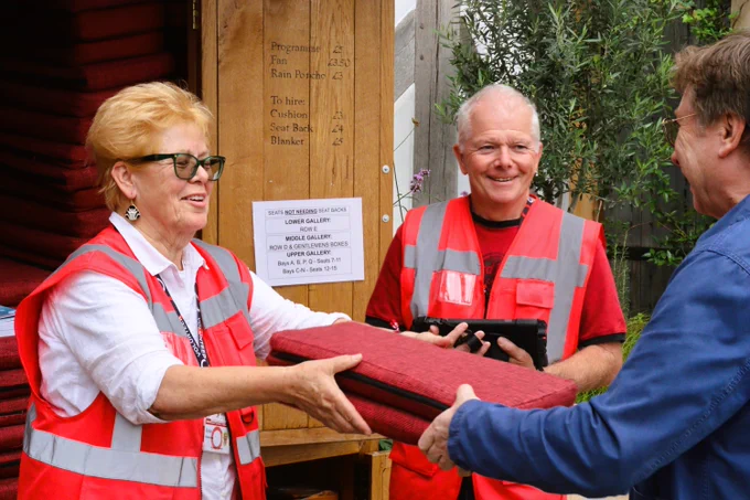 Two volunteer stewards pass out seat cushions outside the Globe Theatre.  