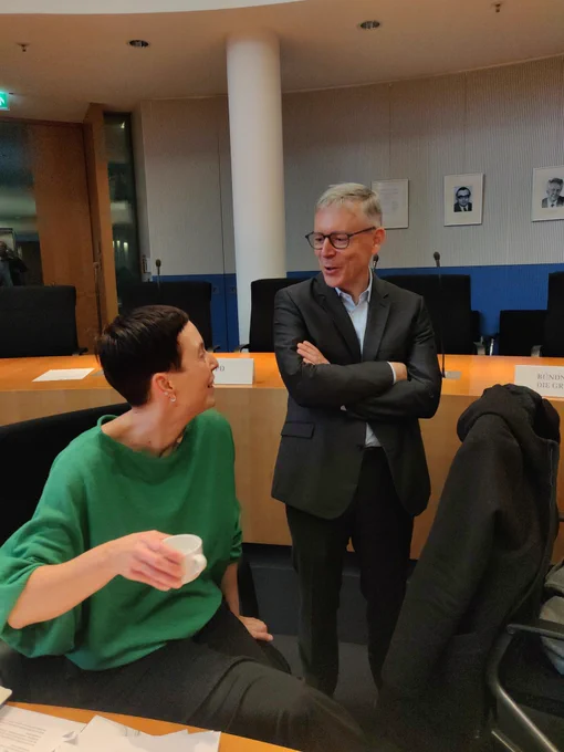Peter Ganten steht im Ausschusssaal neben Jutta Horstmann vom ZenDiS (sitzend), die beiden sind einander zugewandt und miteinander im Gespräch