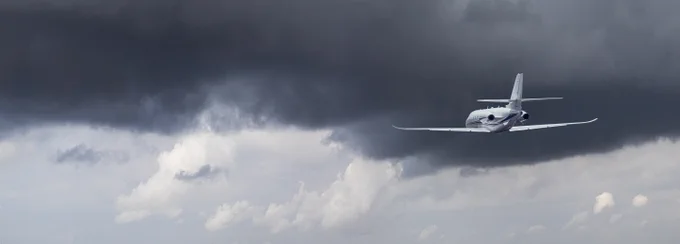 This photo features an airplane, seen to the right side of the image, flying below a dark cloudy sky.
