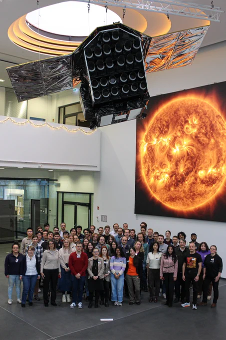group picture taken under a hanging model of the PLATO spacecraft