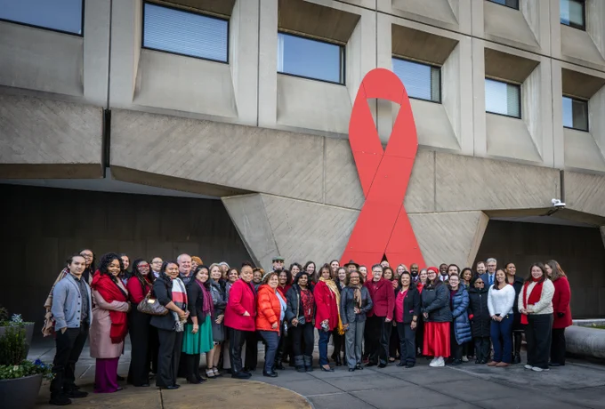 A group photo of HUD Agency Head Adrianne Todman with several HUD employees outside of the HUD headquarters with the red ribbon in the background.