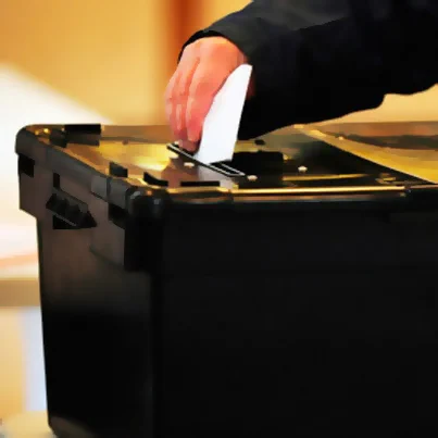A hand placing a ballot paper in a ballot box.