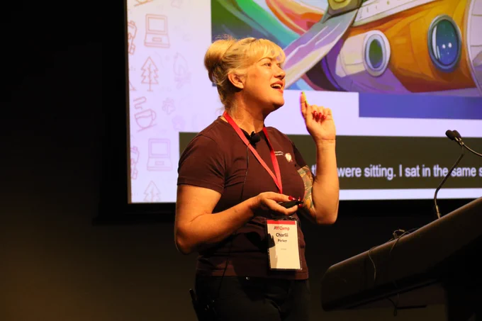 Charlii Parker speaking animatedly during her presentation at A11y Camp, with slides on the big screen behind her.