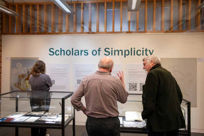 Three people stood looking at the Scholars of Simplicity exhibition
