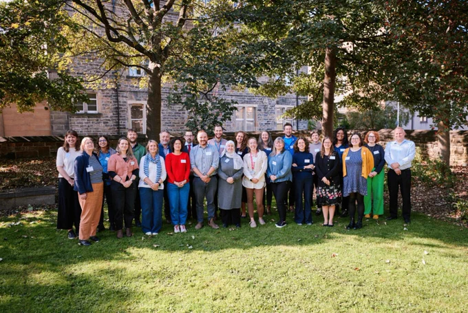 PSCAN members at their latest in person gathering in autumn 2024. A group of people standing on some grass, under some trees in the sunshine. 