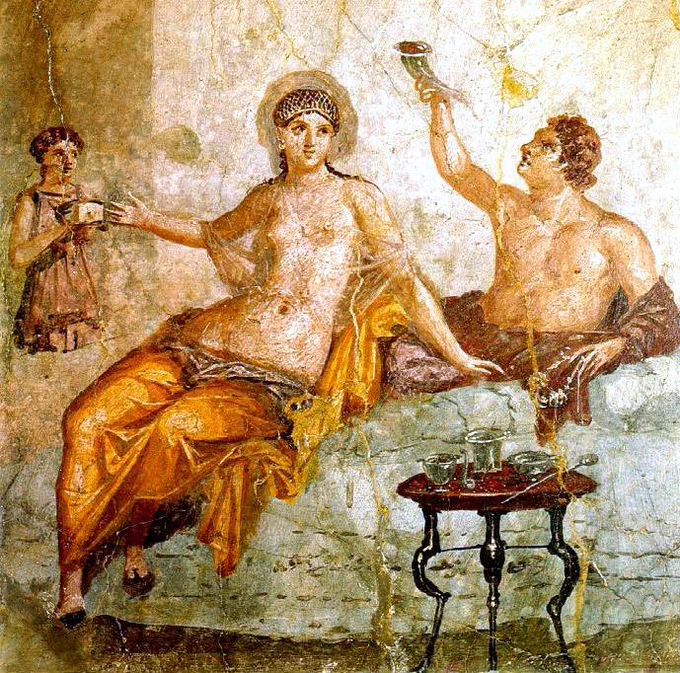 Fresco from Herculaneum depicting a Roman banquet. A woman in a golden robe but nude from the waist up reclines with man dressed in reddish brown robes who is likewise nude from the waist up. In the foreground is a small table with three legs. An (likely enslaved) attendant stands off to one side. Museo Archeologico Nazionale di Napoli, accession number (inv. 9024). Source: World History Encyclopaedia