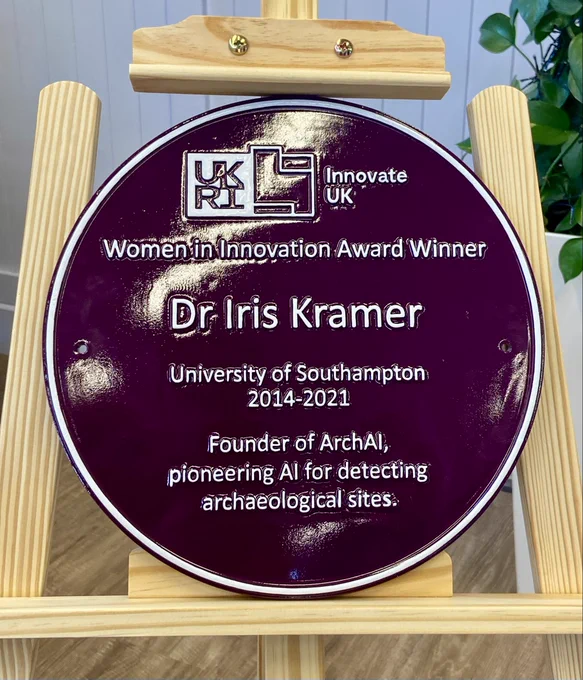 Close-up of the purple plaque: A close-up view of the purple plaque mounted on a wooden easel. The plaque reads: "Women in Innovation Award Winner Dr Iris Kramer, University of Southampton 2014–2021, Founder of ArchAI, pioneering AI for detecting archaeological sites.