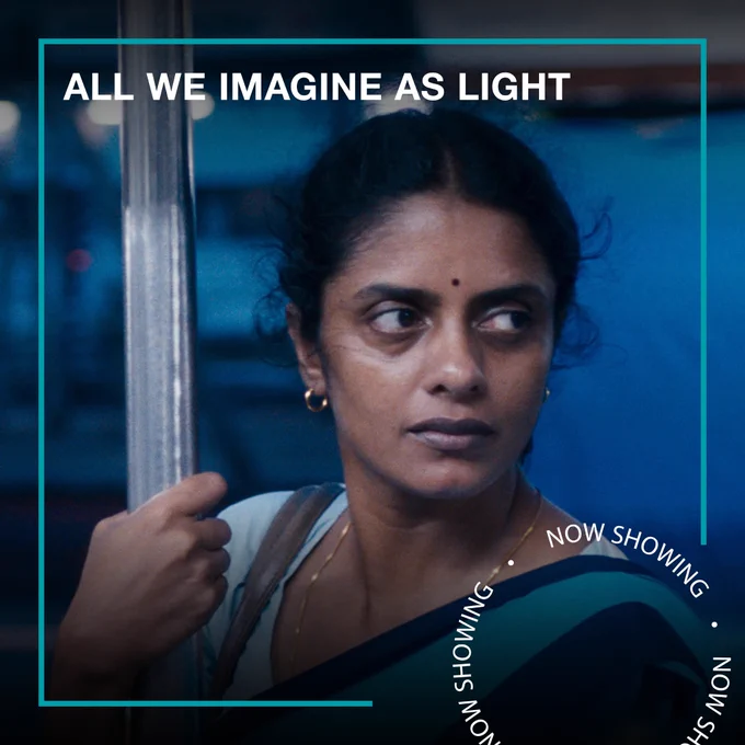 A woman holds on to a pole while standing in a subway, looking into the distance. Text - All We Imagine as Light, Now Showing.