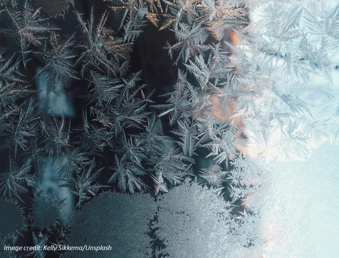 Photograph of frost crystals spreading across a glass windowpane. Image has been rotated 90 degrees clockwise from original orientation. Image credit: Kelly Sikkema/Unsplash