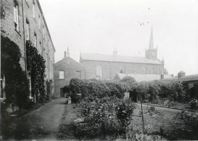 Black and white photograph of an enclosed garden, with a nineteenth-century church in the background.