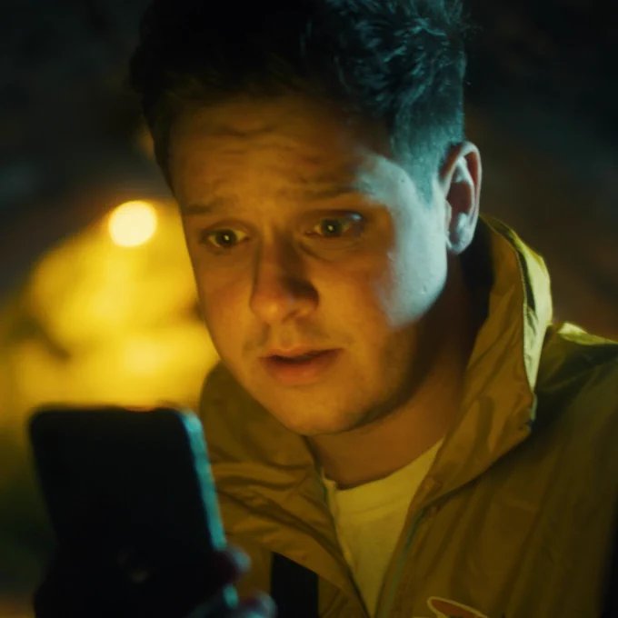 Still from Secrets of a Wallaby Boy: Tim (Brandon McCaffrey) is in a dark alleyway, looking into his phone, concerned.