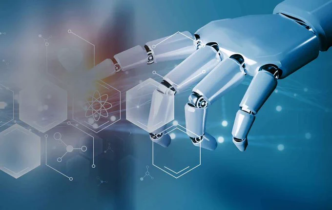 Blue background. Robotic white hand reaching out and one of the fingers is touching a hexagon shape. There are a series of hexagon shapes on the left side of the screen. Most are filled. One has an atom icon in it. Credit: Have a Nice Day Photo/Shutterstock