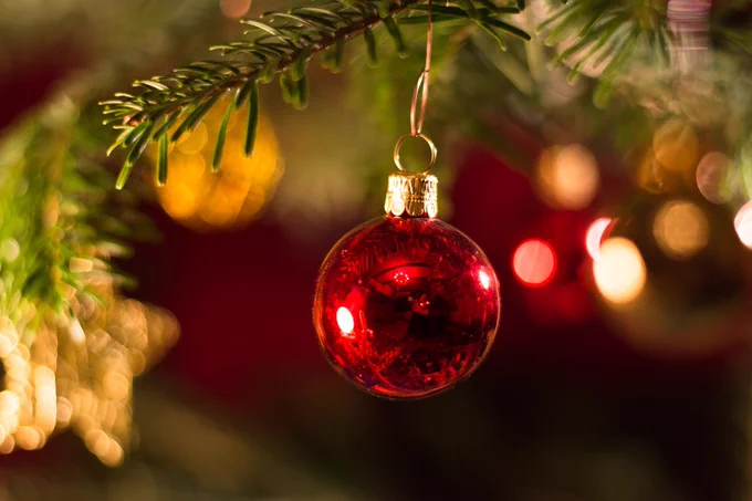 A close up of a shiny red metallic bauble hanging from a green Christmas tree