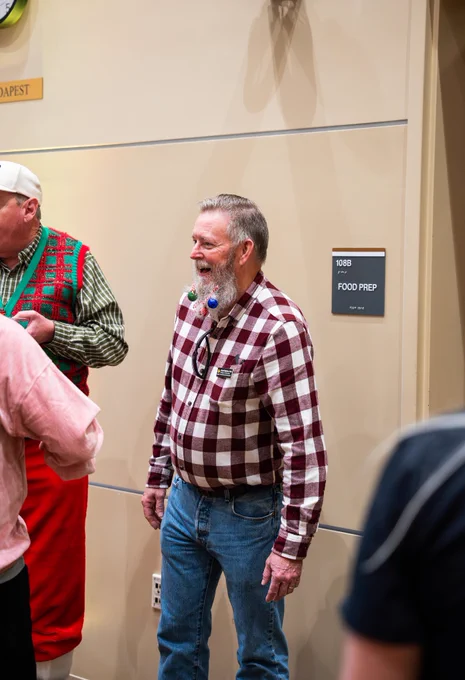 A UCF College of Community Innovation and Education faculty member with ornaments in his beard is smiling and interacting with other faculty and staff.