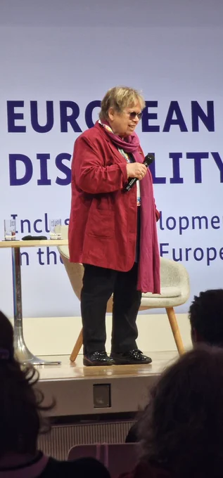 Hannelore Loskill, Chairwoman of the Speakers' Council of the German Disability Council, speaking on the stage of the European Regional Disability Summit. Behind her is a sign with the title of the event.