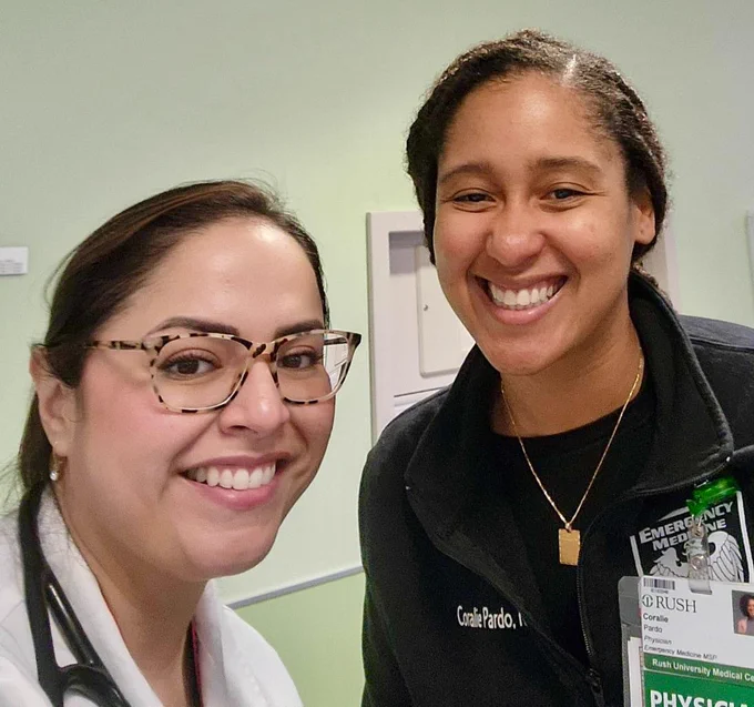 Susan Lopez, MD, and Coralie Pardo, MD, smiling in a hospital setting, one wearing a white coat and glasses, the other in an emergency medicine jacket.