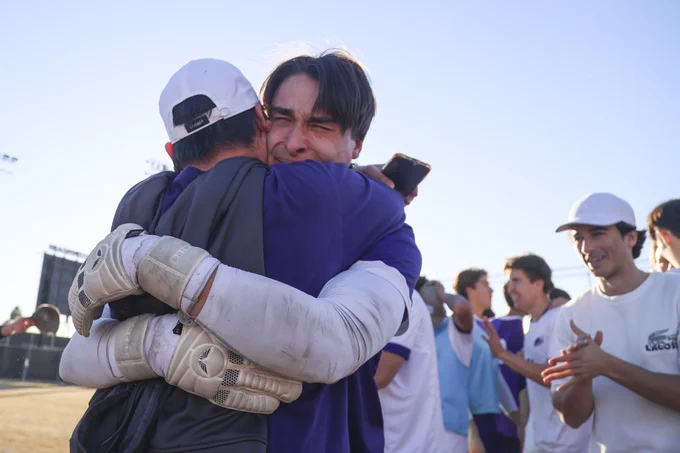 A tearful Max Landa '25 and a fellow team member embrace joyfully on a sunny field after the national championship win. Other players appear in the background, celebrating.