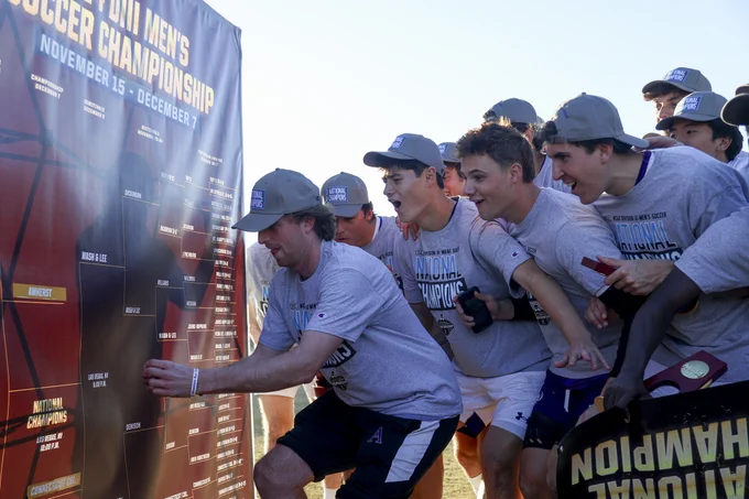 The Amherst College men's soccer team place themselves as the winners of the national championship on the NCAA Men's Soccer Championship bracket, wearing championship hats and t-shirts.