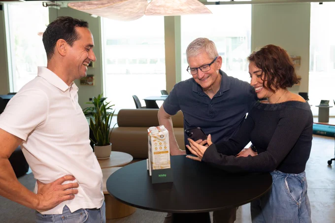 Tim and the developers of eJaby stand around a tall, round, black table, looking at the app on iPhone.