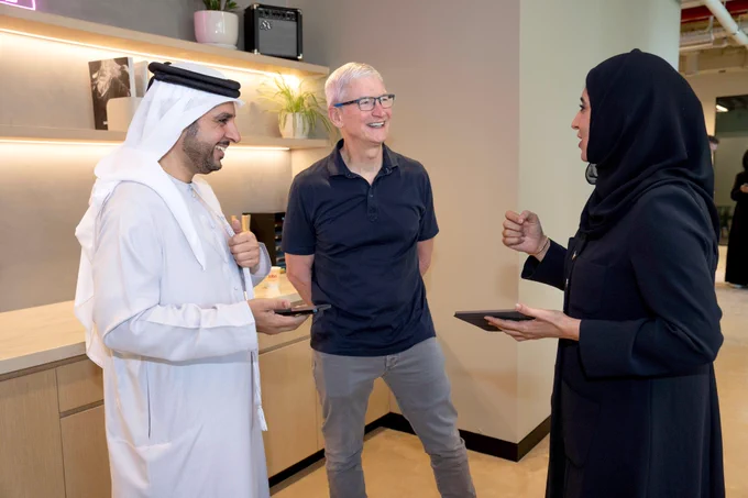 The developers of Drivu stand on either side of Tim, holding iPhone and iPad while chatting.