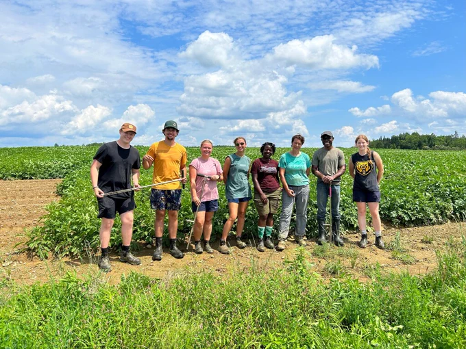 Group of people standing in front of a field, holding soil probes. 