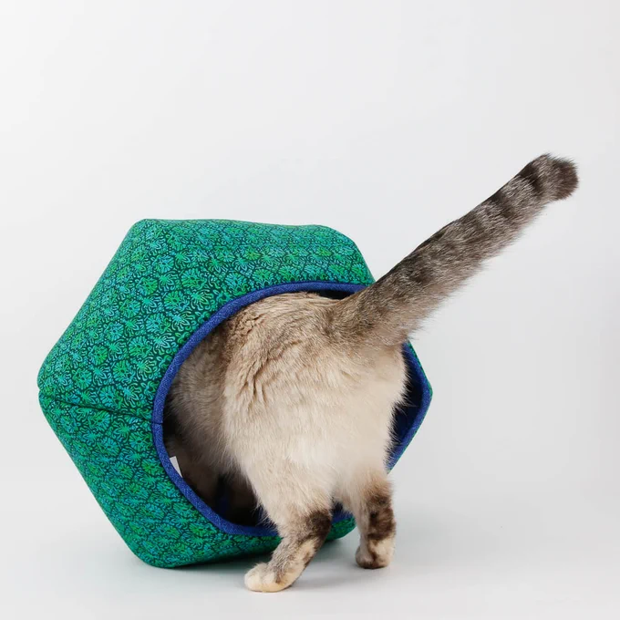 A small cat peeks into the Cat Ball® cat bed, made in a bold blue and green foulard print. 