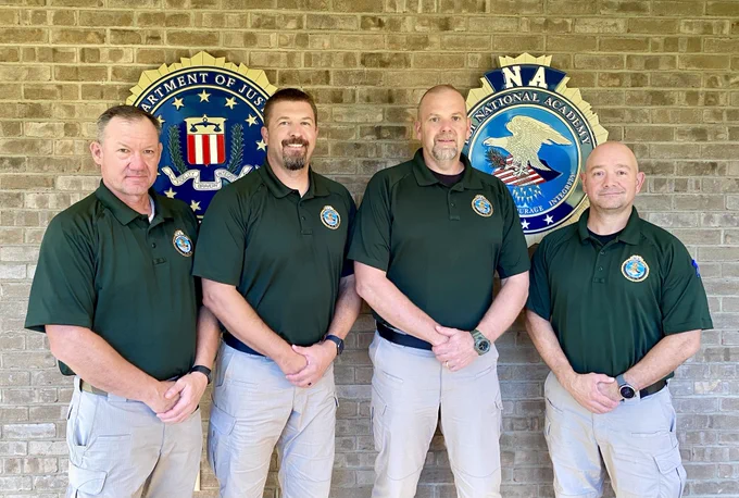 photo of 4 men in green polo shirts posing in front of the FBI seal and National Academy seal 