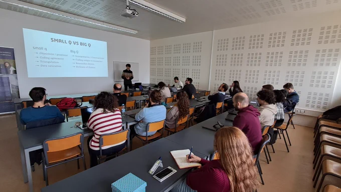 David with a slide on the background reading "small q vs BIG Q" and some distinctions between the two approaches. a room with ~15 group members listening carefully.