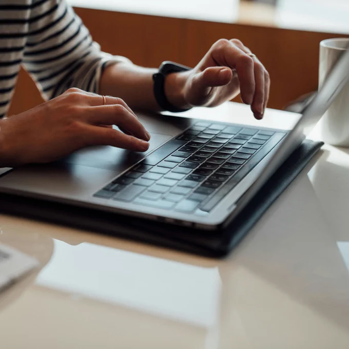 Person clicking on a Mac laptop with a coffee cup next to it