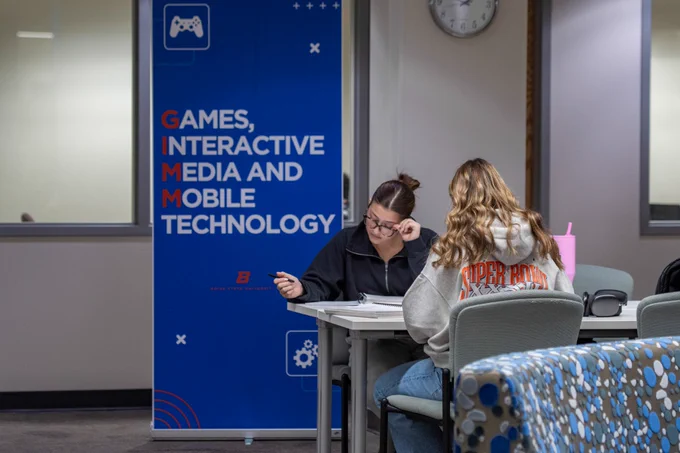 Boise State students working near a GIMM banner inside Albertsons Library.