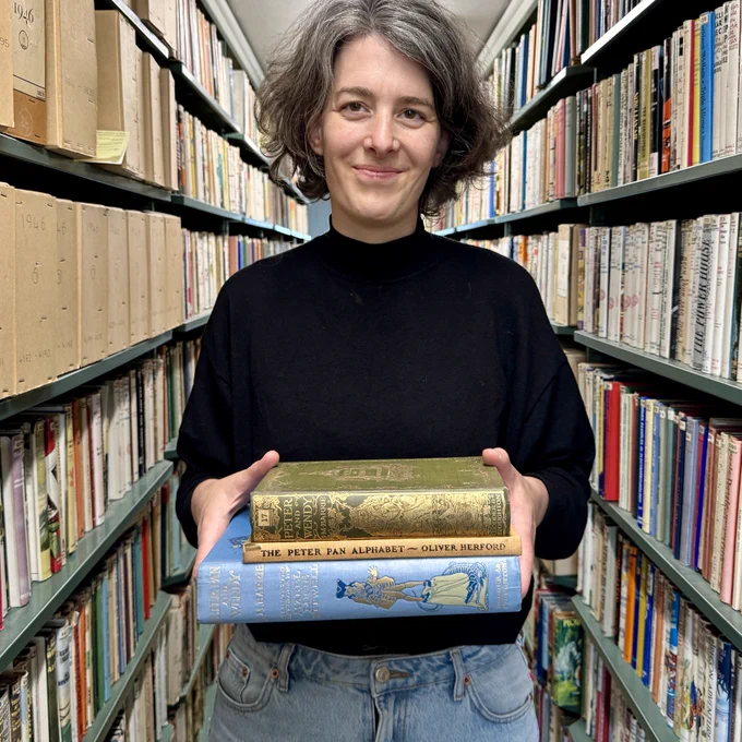 Photograph of Dr Sarah Pyke, 2024 Munby Fellow. They are holding a pile of books. 